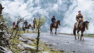 In vernebelten Bergen reiten vier Männer auf Pferden.